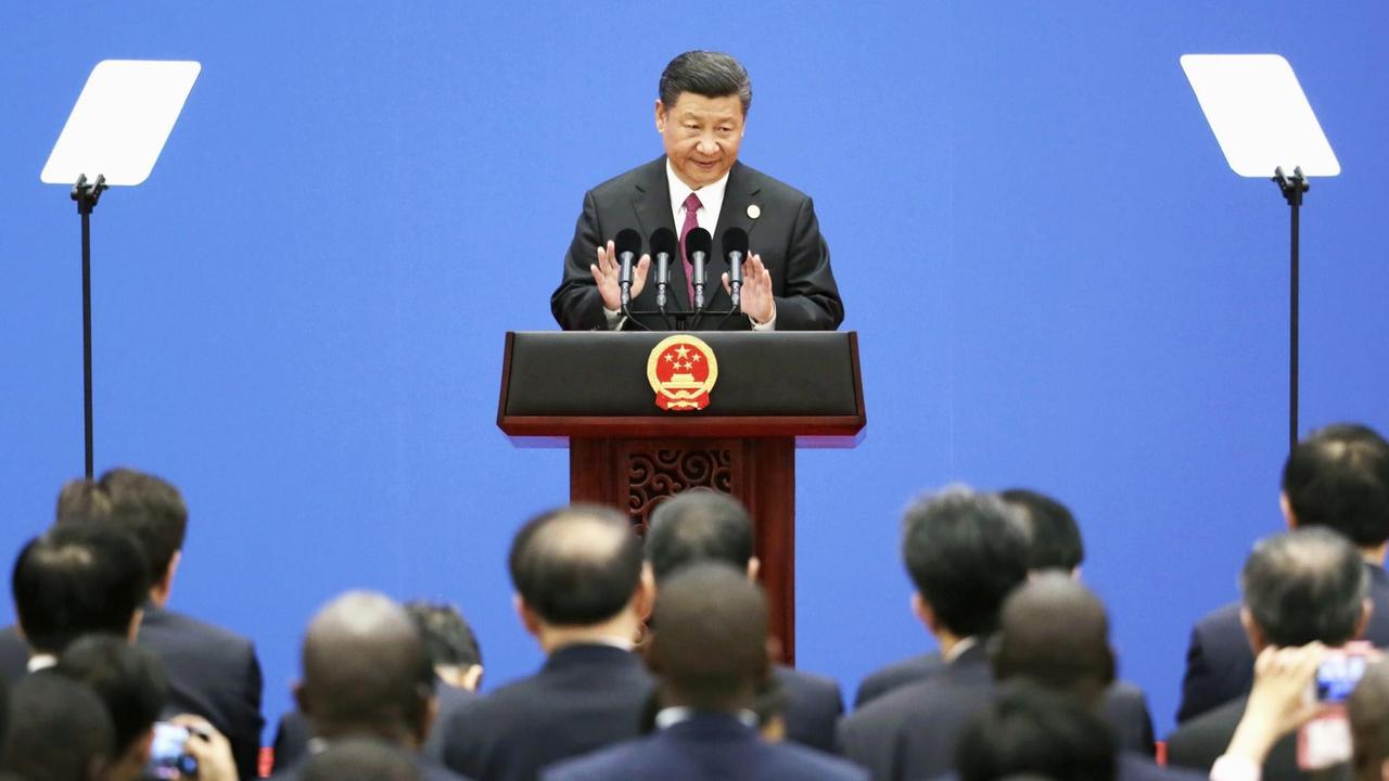 Der chinesische Staatspräsident Xi Jinping steht redend und gestikulierend hinter einem Pult und spricht zu einer Menschenmenge vor ihm.