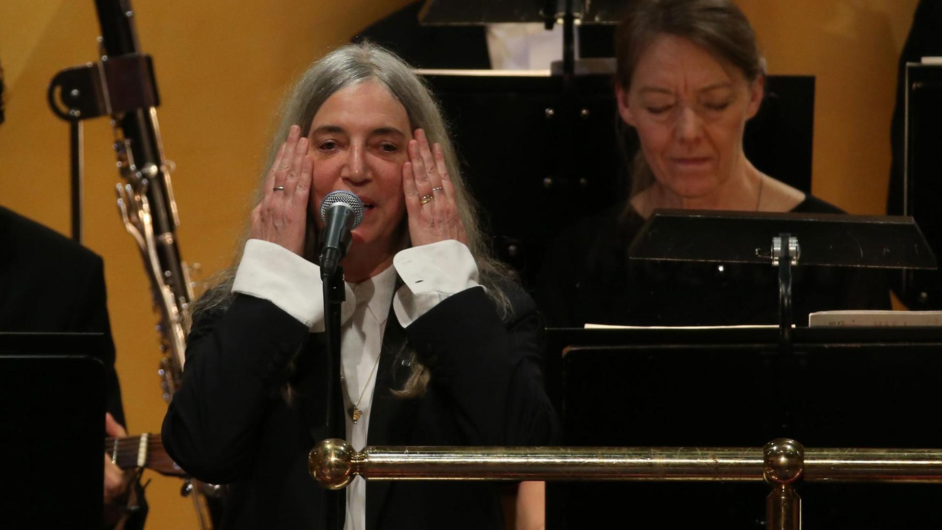 Die Sängerin steht vor einem Mikrofon und hält sich ihre beiden Hände seitlich ans Gesicht. 