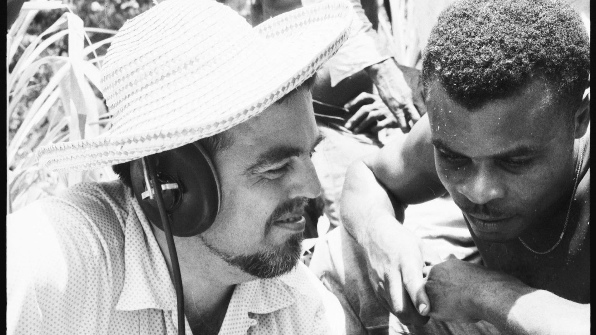 Alan Lomax (links) und Musiker während des Abhörens einer Aufnahme in der Karibik. Alan Lomax trägt Kopfhörer
