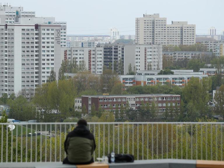 Ein Mann sitzt allein auf einer Terrasse und schaut zu den Plattenbauten von Marzahn hinüber, die zu DDR-Zeiten errichtet wurden.