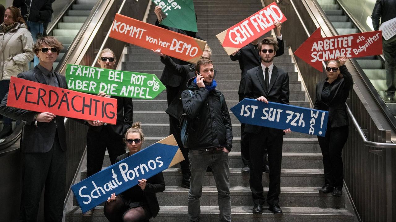 Demonstranten halten Schilder mit Aufschriften wie "geht fremd", "Schaut Pornos", "fährt über die rote Ampel". Aktion gegen den Ausbau von Videoüberwachung im öffentlichen Raum am Bahnhof Südkreuz in Berlin am 27.11.2017. 