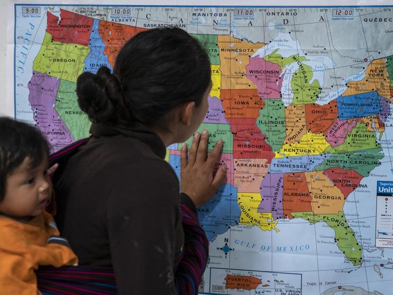 Ein Frau aus Guatemala, die ihr Kind in einem Tragetuch auf dem Rücken trägt, schaut auf eine Karte der USA; Zentrum für Flüchtlinge der Hilfsorganisation Annunciation House