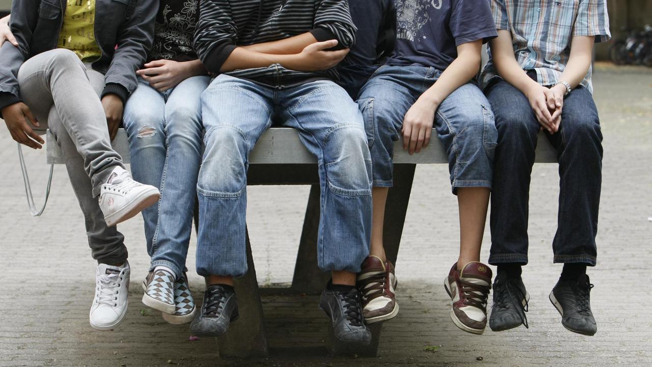 Schüler an einem Gymnasium sitzen nebeneinander auf einer Tischtennis-Platte.