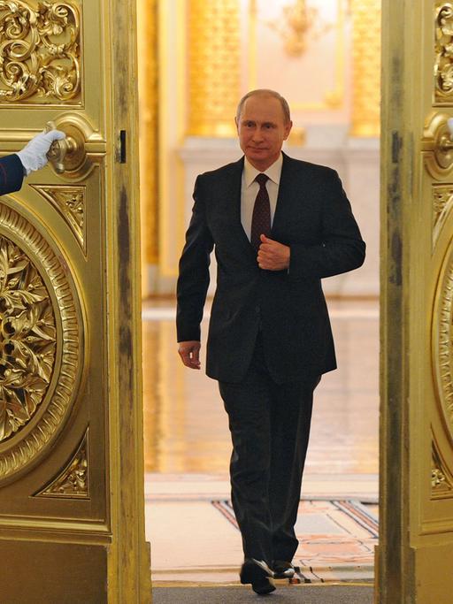 Wladimir Putin schreitet durch eine goldbesetzte Flügeltür, die ihm von zwei Uniformierten geöffnet wird, zu seiner Rede.