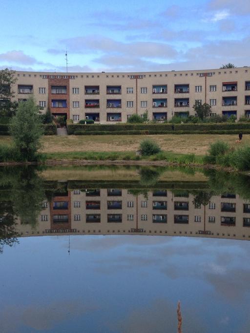 Das Bild zeigt hufeisenförmig angeordnete Häuser im Halbrund um einen See, der im Vordergrund ist. Die Hufeisensiedlung in Berlin-Britz.