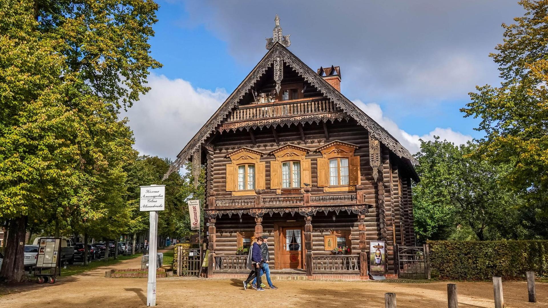 Ein Holzhaus in der Russischen Kolonie Alexandrowka in Potsdam. Davor sind zwei Spaziergänger.
