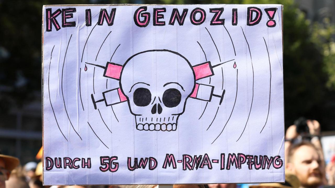 Bei einer Demonstration gegen die Pandemiemaßnahmen ist ein Plakat zu sehen, dass sich gegen einen behaupteten Genozid durch den Mobilfunkstandard 5G und Impfungen wendet.