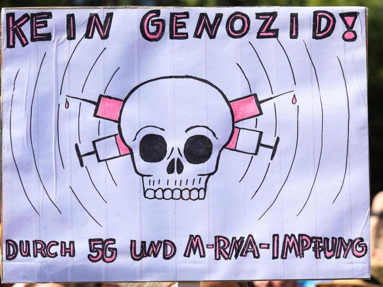 Bei einer Demonstration gegen die Pandemiemaßnahmen ist ein Plakat zu sehen, dass sich gegen einen behaupteten Genozid durch den Mobilfunkstandard 5G und Impfungen wendet.