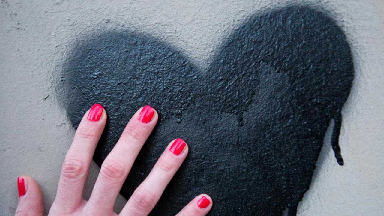 Eine Frauenhand mit rot lackierten Fingernägeln berührt am 03.03.2014 in Berlin ein schwarzes Herz, das auf eine Mauer gespüht wurde.