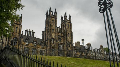 Blick auf das historische Gebäude des New College der University of Edinburgh, dahinter ein grauer Wolkenhimmel.