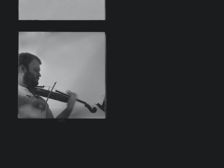Ein Mann spielt hinter einem Fenster Geige.