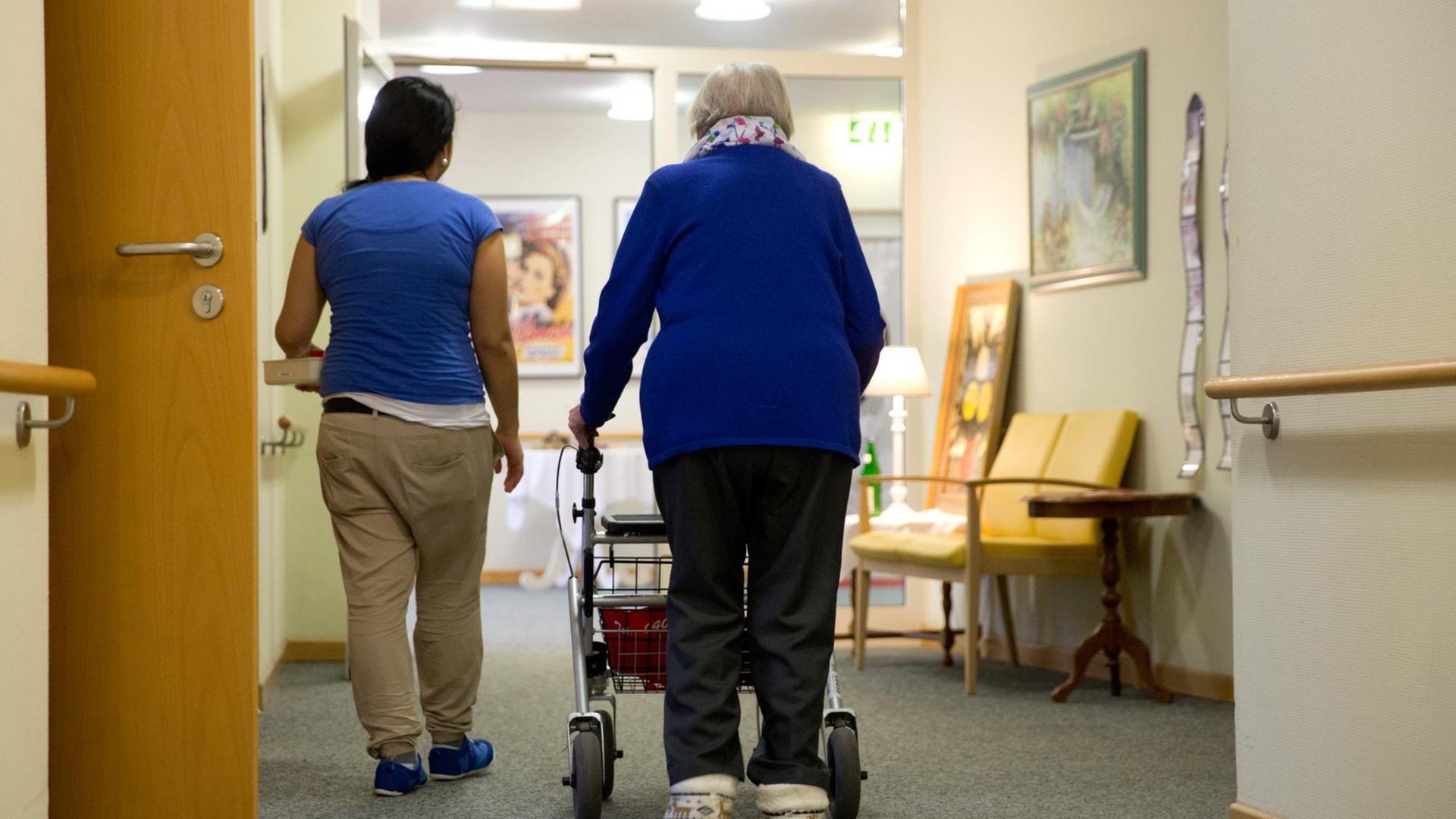 Eine Pflegerinn begleitet am 12.02.2015 in Hamburg eine Bewohnerin eines Seniorenwohnheims mit ihrer Gehhilfe (Rollator).
