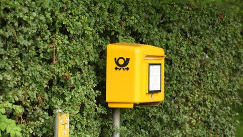 Ein Postkasten der Deutschen Post steht in Timmendorfer Strand vor einer grünen Hecke.