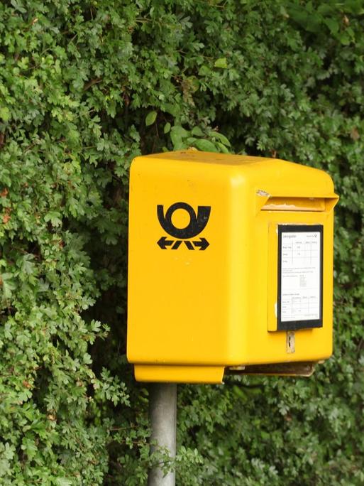 Ein Postkasten der Deutschen Post steht in Timmendorfer Strand vor einer grünen Hecke.