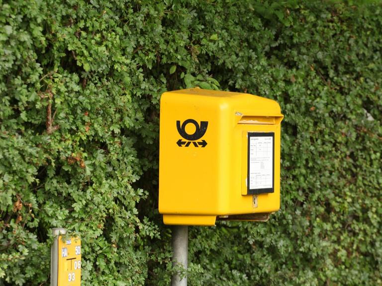 Ein Postkasten der Deutschen Post steht in Timmendorfer Strand vor einer grünen Hecke.