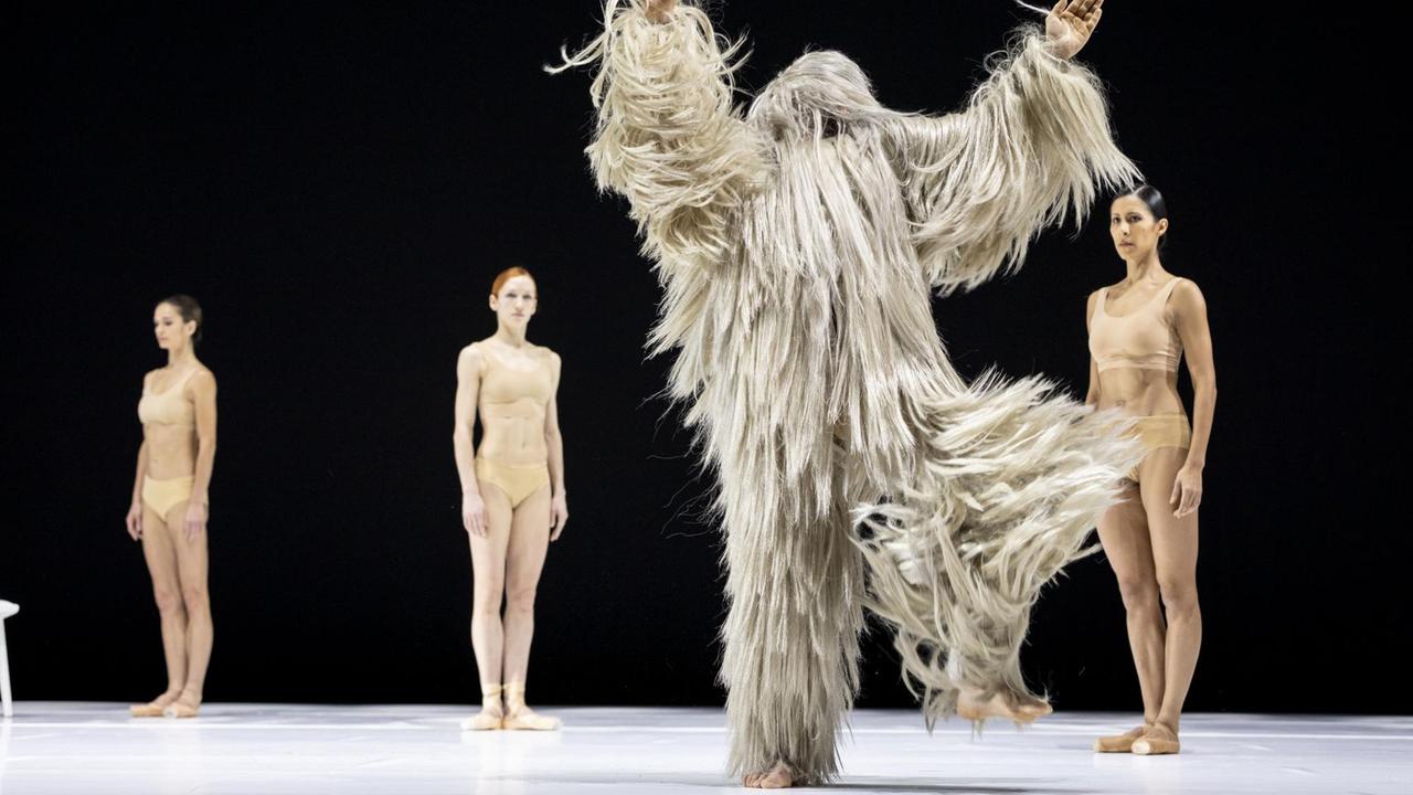 Im Szenenbild der Tanzperformance "LIB" stehen drei Tänzerinnen und ein Darsteller in Fellkostüm auf der Bühne. 