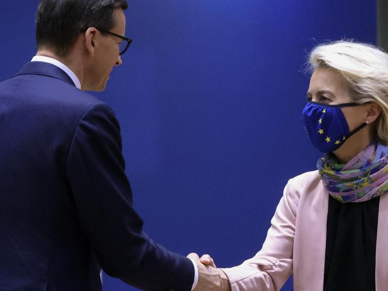 Mateusz Morawiecki und Ursula von der Leyen schütteln einander die Hände. Sie trägt dabei eine Maske mit dem Logo der EU.