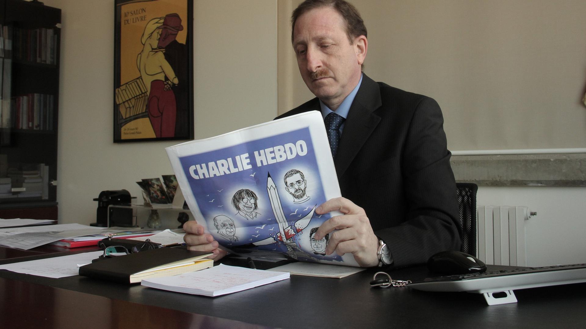 Er hält die aktuelle Ausgabe des Magazins in der Hand, mit der das Blatt auf die Charlie-Hebdo-Anschläge reagiert.