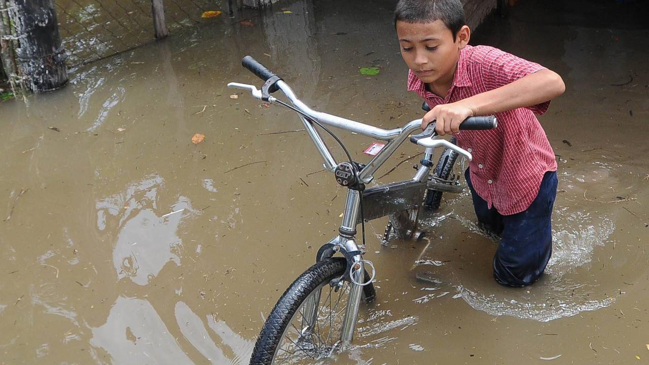 Ein Junge im rotkarierten Hemd kämpft sich mit seinem Fahrrad durch eine überschwemmte Straße in Honduras. .