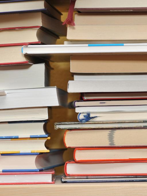 Mehrere Bücher liegen auf drei Stapeln nebeneinander.