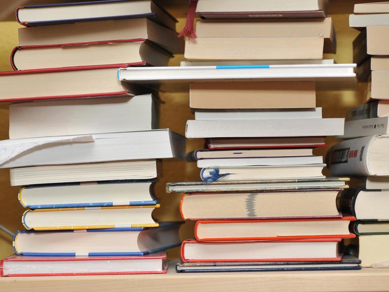 Mehrere Bücher liegen auf drei Stapeln nebeneinander.