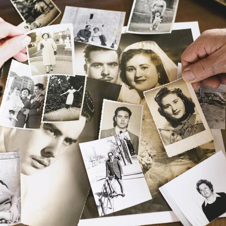 Das Bild zeigt einen Tisch voller alter schwarz-weiss Fotos sowie die Hände von Senioren, die Bilder auswählen.