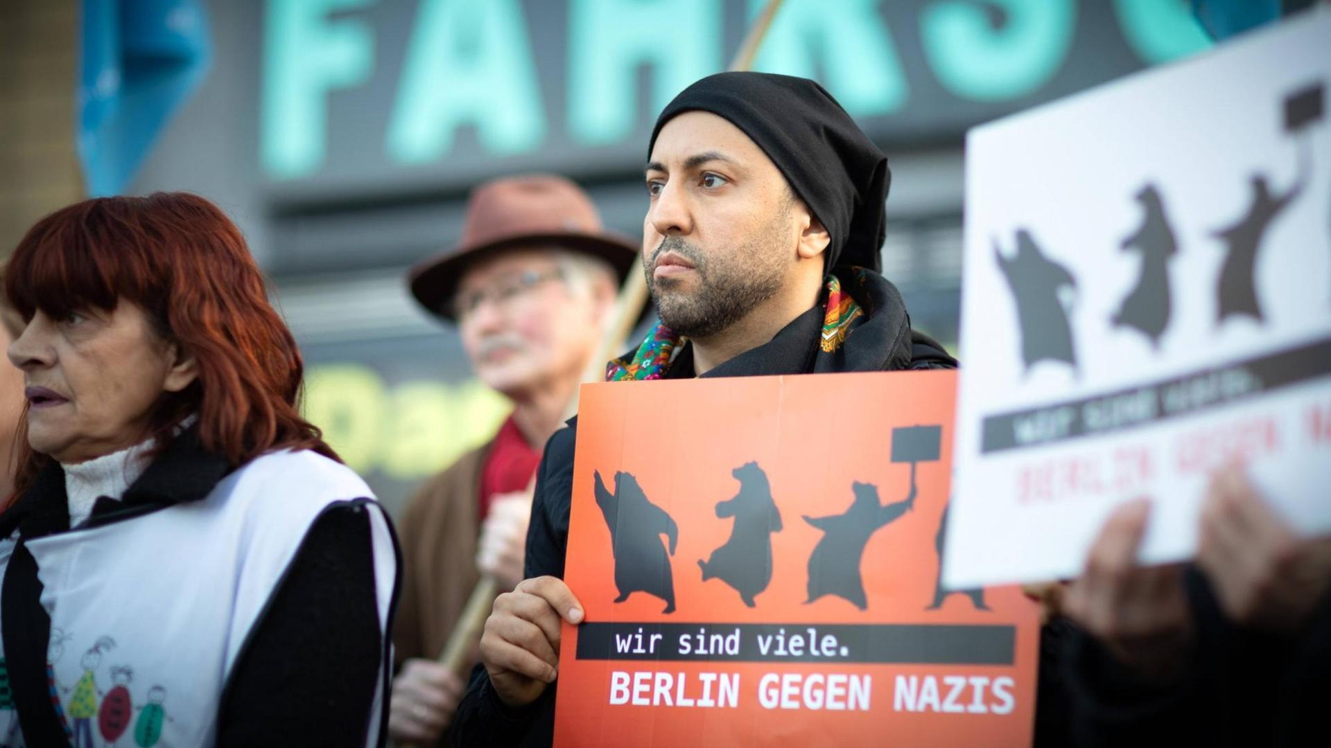 Ferat Kocak steht in einer Kundgebung in Berlin-Neukölln mit einem Schild auf dem steht: Wir sind mehr. Berlin gegen Nazis.