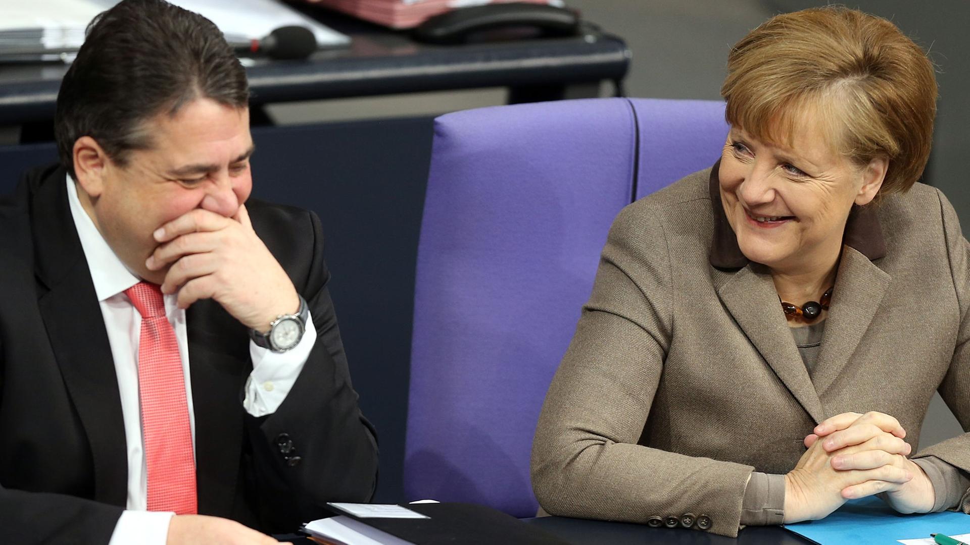 Bundeswirtschaftsminister Sigmar Gabriel (SPD) und Bundeskanzlerin Angela Merkel (CDU) lachen auf ihren Sitzen während einer Debatte im Bundestag.