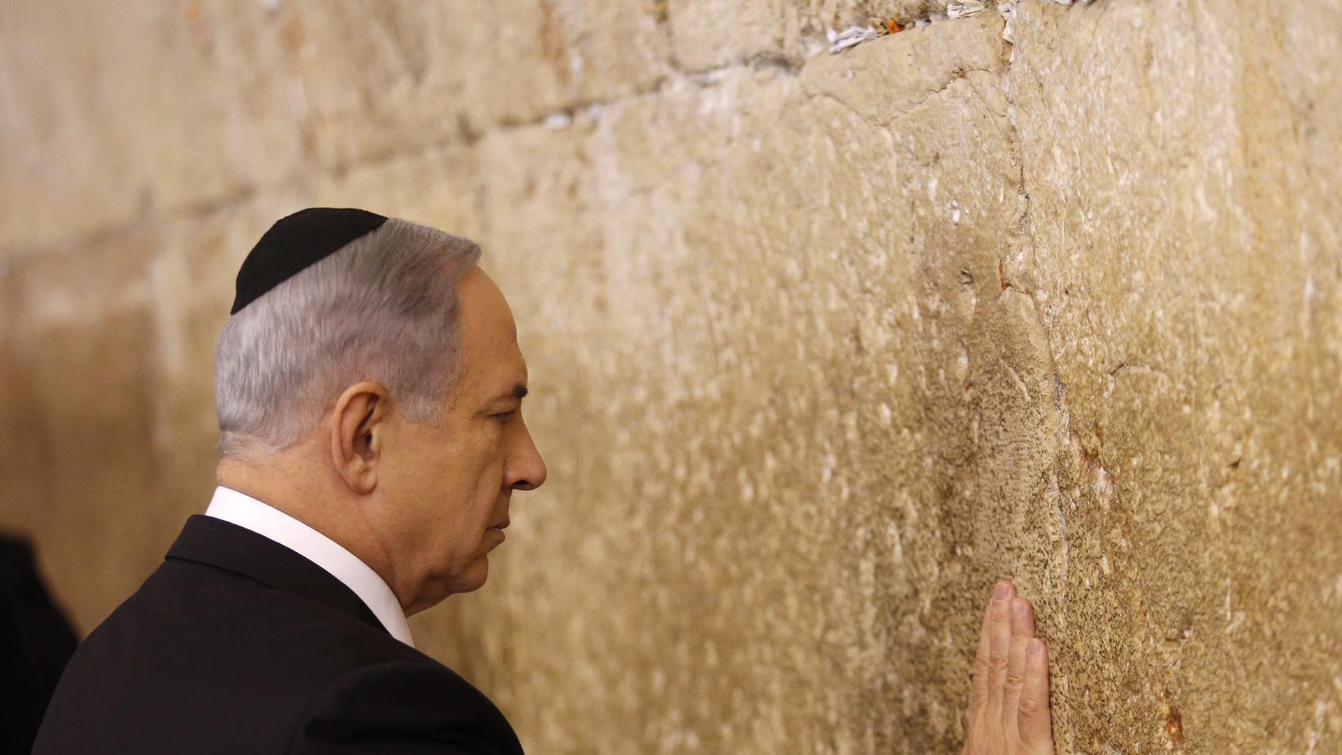 Israels Premier Benjamin Netanjahu in Anzug und Kippa berührt mit der Handfläche die Klagemauer in der Altstadt von Jerusalem.