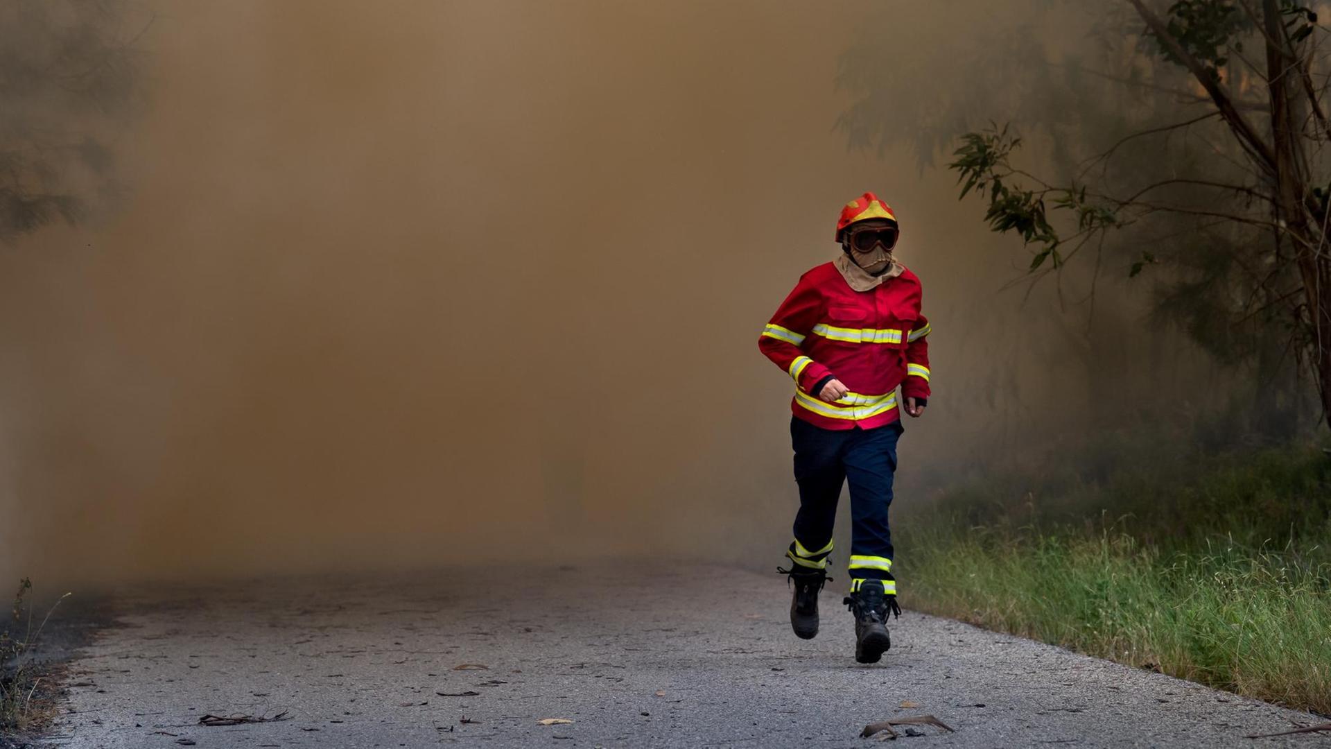 Ein Feuerwehrmann läuft am 19.06.2017 etwa 160 Kilometer Nordöstlich von Lissabon (Portugal) nahe der Ortschaft Vale Verde aus dem Feuerrauch heraus. Der verheerende Waldbrand mit mehreren Toten in Portugal ist der Polizei zufolge durch Blitzschlag ausgelöst worden.