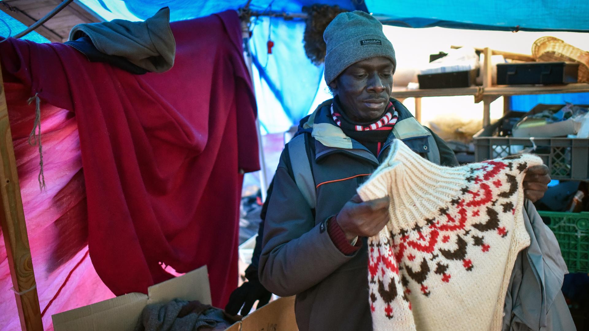 Ein Flüchtling begutachtet am 11.12.2014 in Hannover Winterkleidung in einem Zelt eines provisorischen Flüchtlingscamps.