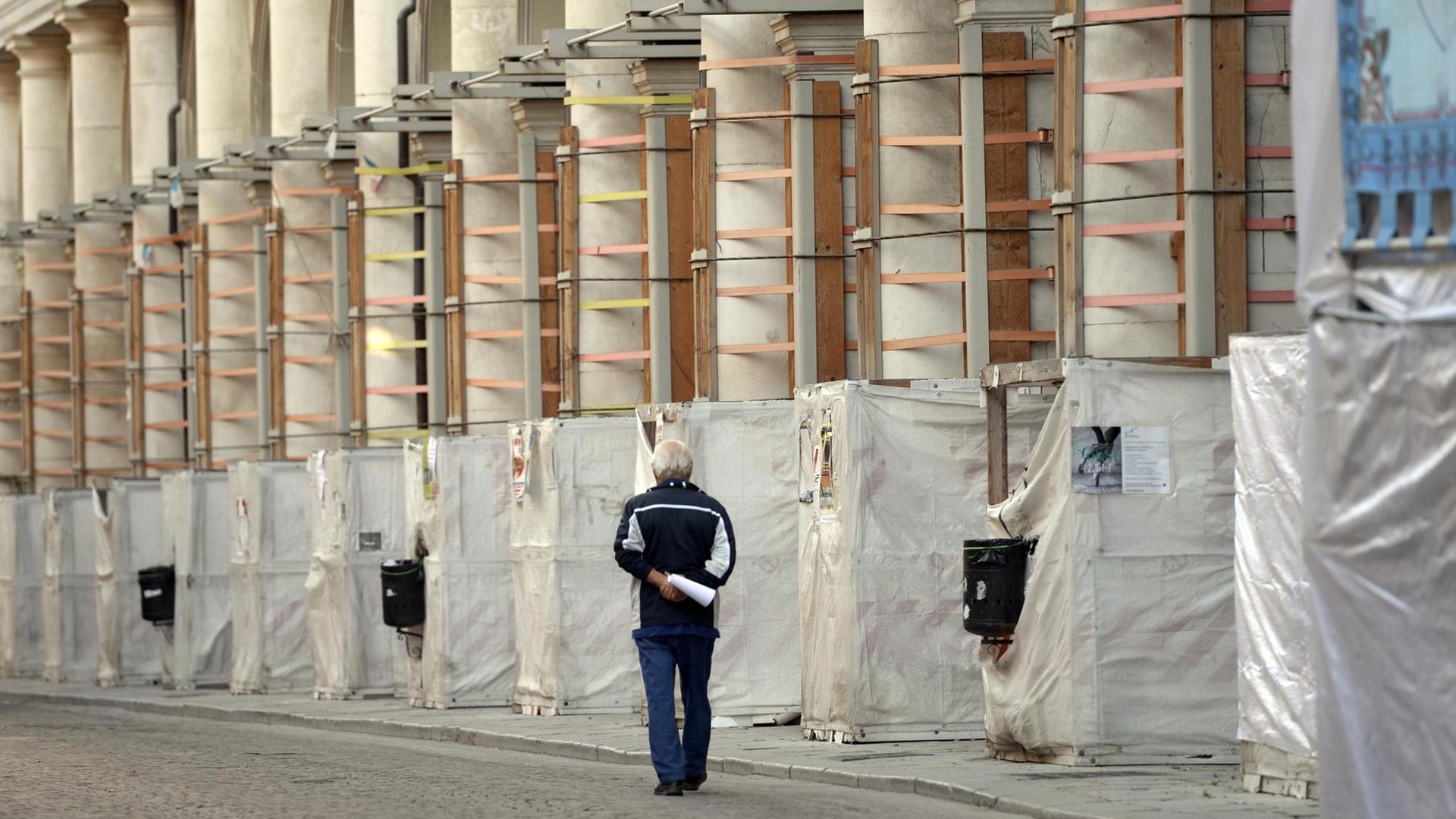 Ein Mann geht an einem eingerüsteten historischen Gebäude mit Säulen vorbei Foto: Maurizio Gambarini/dpa 