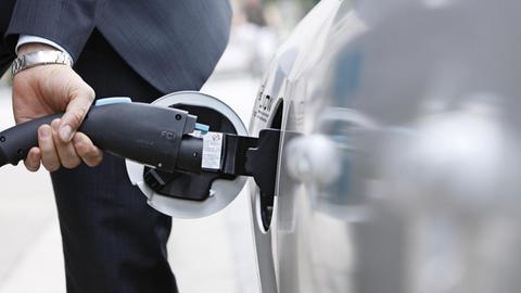 Das Bild zeigt das Aufladen eines E-Autos mit einem Stecker. 