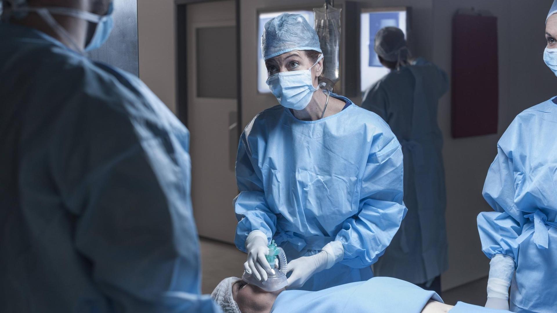 Ein Operationsteam im Krankenhaus. Eine Frau auf der Liege bekommt ein Beatmungsgerät aufgesetzt.
