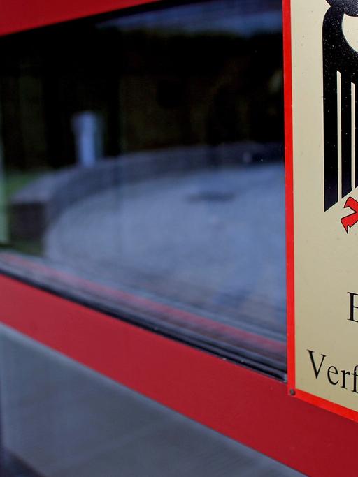 Schild des Bundesamts für Verfassungsschutz mit dem Bundesadler an einer Eingangstür des Gebäudes, durch die eine Frau geht.