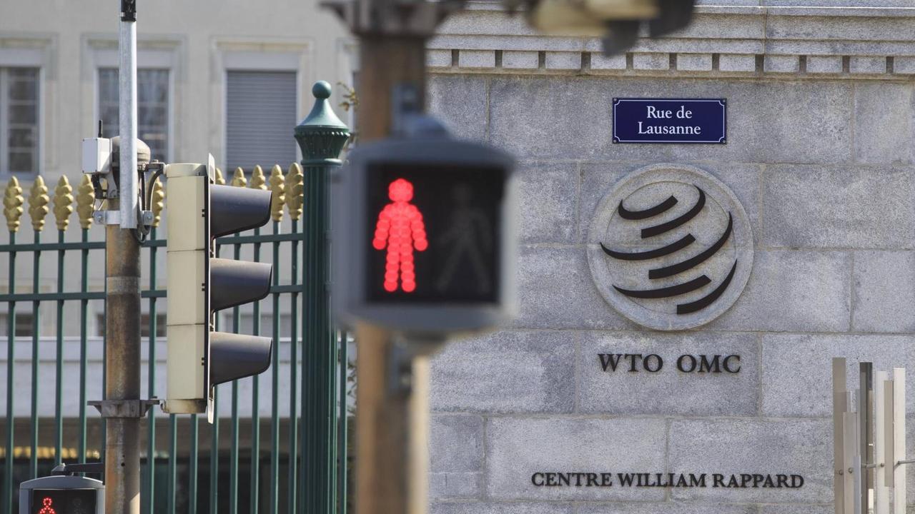 Logo der Welthandelsorganisation WTO am Eingang zum WTO-Gebäude in Genf, im Vordergrund eine Ampel
