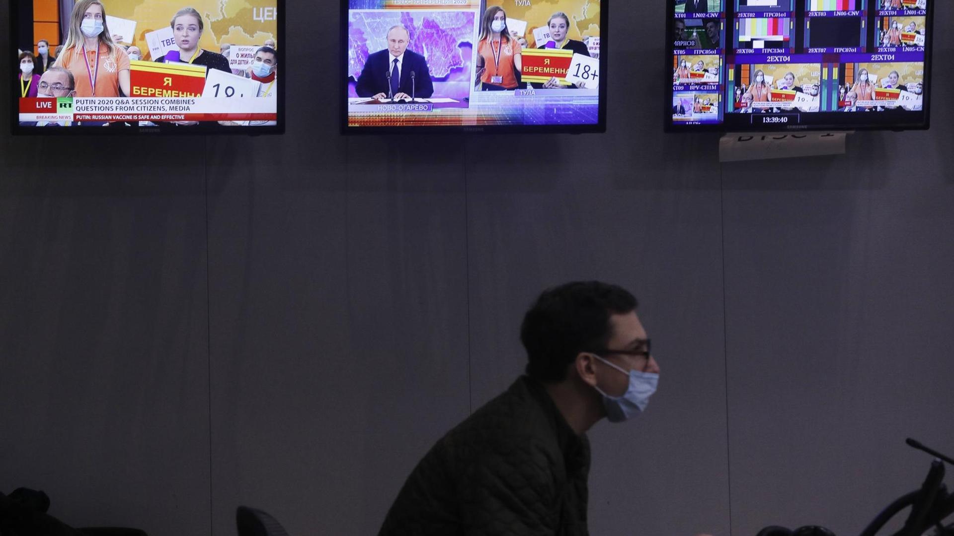 Ein Journalist sitz in einer Redaktion und schaut auf einen Computer. Im Hintergrund sind Bildschirme zu sehen.
