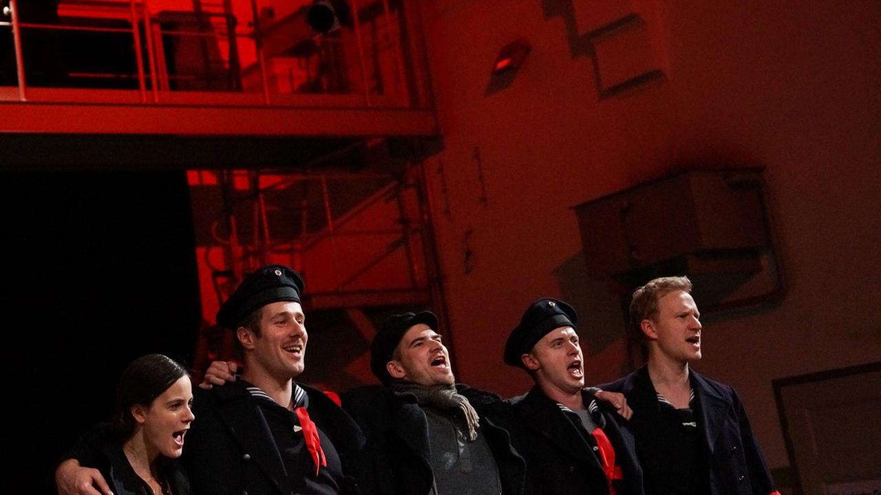 Matrosen und eine Matrosin Arm in Arm auf der in Rot getauchten Bühne des Schauspiel Kiel
