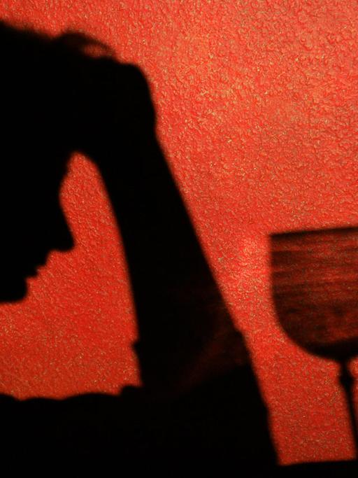 Der Schatten einer Frau, die nachdenklich vor einem Glas Wein sitzt,