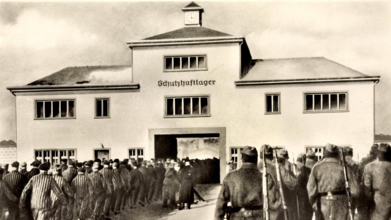 Häftlinge und Wärter stehen vor dem Eingang zum KZ Sachsenhausen. Über dem Tor der Schriftzug: Schutzhaftlager.
