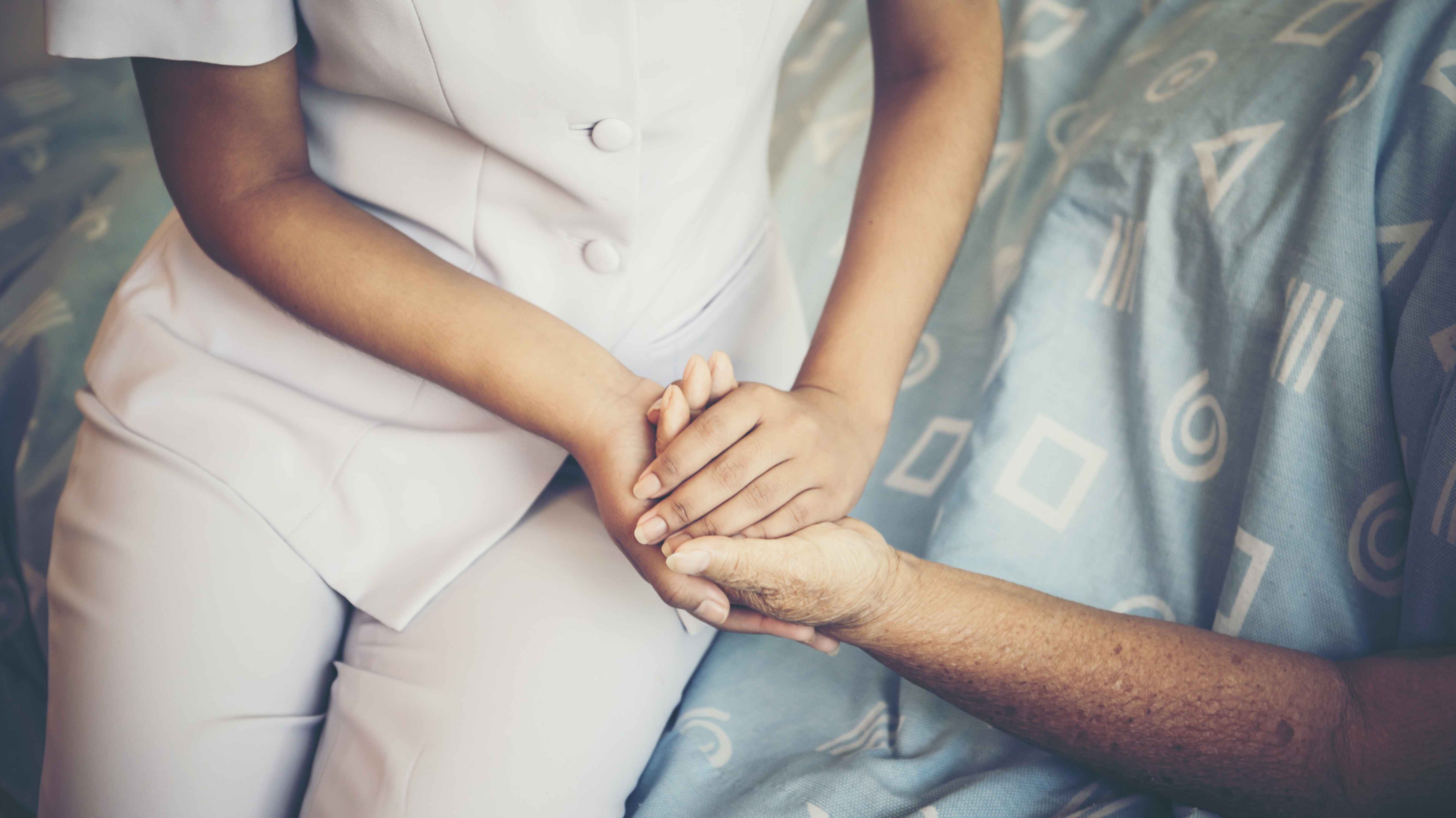 Eine Altenpflegerin hält die Hand einer Bewohnerin.