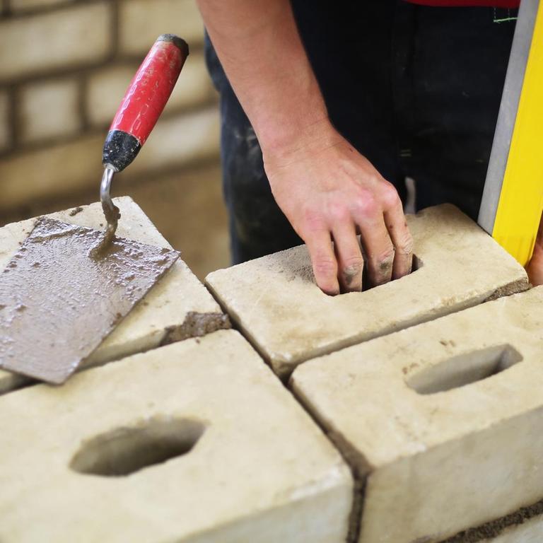 Ein Auszubildender arbeitet an einer Mauer.