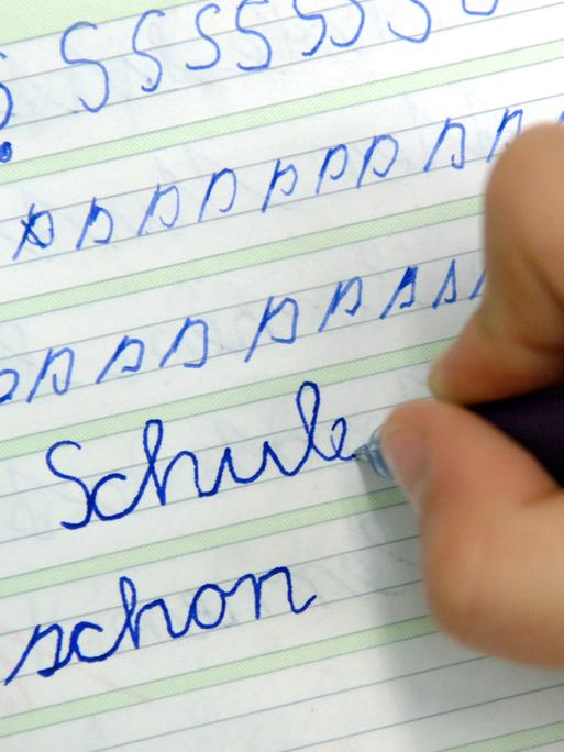 Ein Mädchen schreibt im Unterricht das Wort "Schule" in ihr Heft.