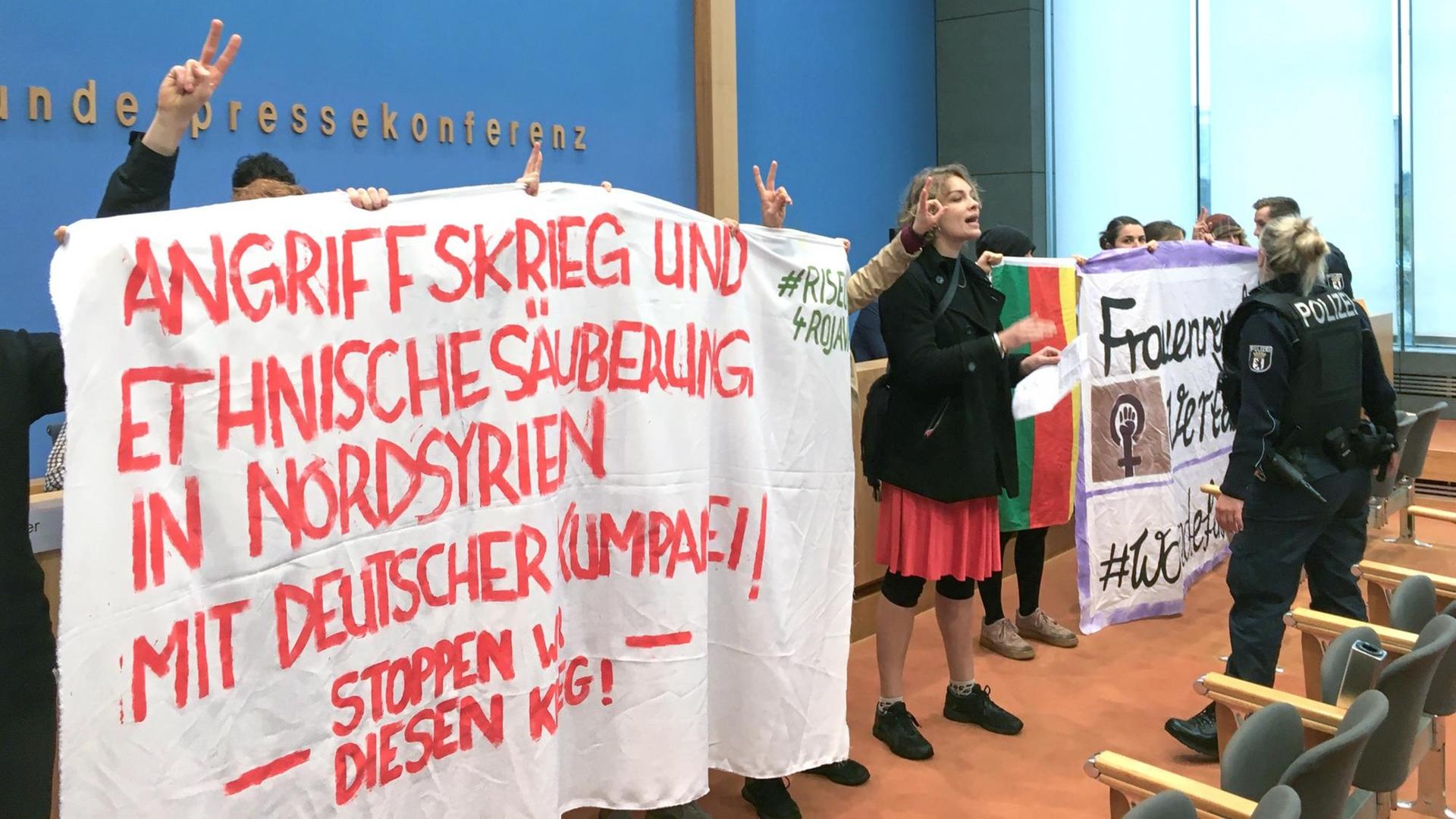 Demonstranten stehen in der Bundespressekonferenz und halten ein Banner mit der Aufschrift «Angriffskrieg und ethnische Säuberung in Nordsyrien mit deutscher Kumpanei. Stoppen wir diesen Krieg!». Demonstranten stehen in der Bundespressekonferenz und halten ein Banner mit der Aufschrift «Angriffskrieg und ethnische Säuberung in Nordsyrien mit deutscher Kumpanei. Stoppen wir diesen Krieg!».