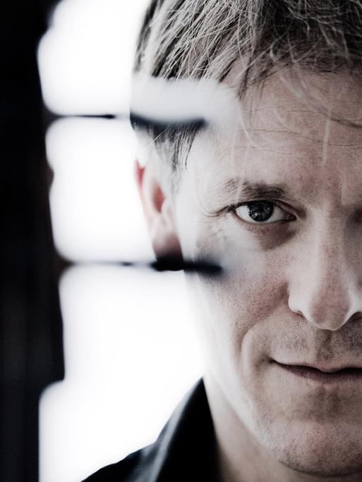 Der Cellist Alban Gerhardt blickt an den Wirbeln seines Instrumentes vorbei in die Kamera.