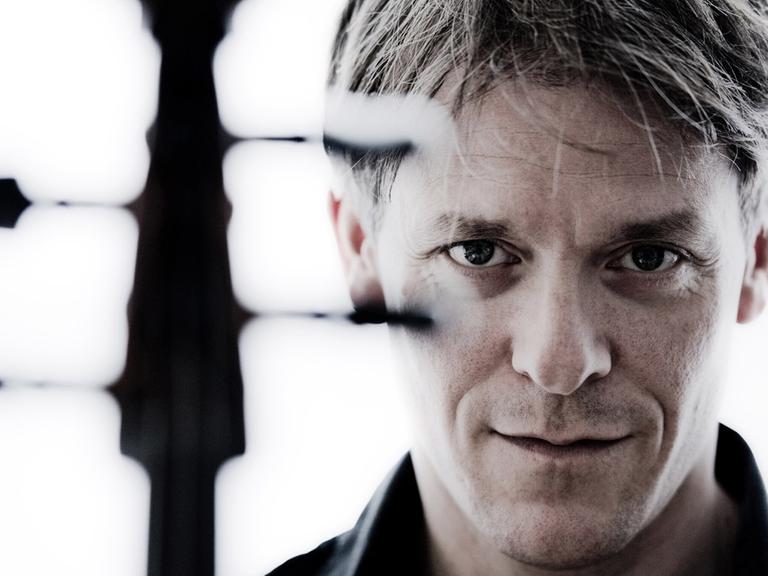Der Cellist Alban Gerhardt blickt an den Wirbeln seines Instrumentes vorbei in die Kamera.