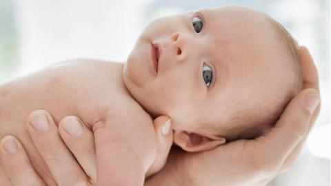 Ein Neugeborenes liegt auf einem männlichen Arm und schaut zur Kamera.