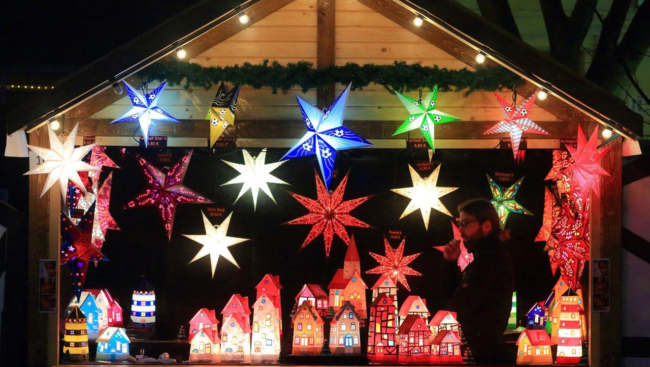 Beleuchtete Papiersterne und Papierhäuser an einem Stand auf dem Weihnachtsmarkt. 