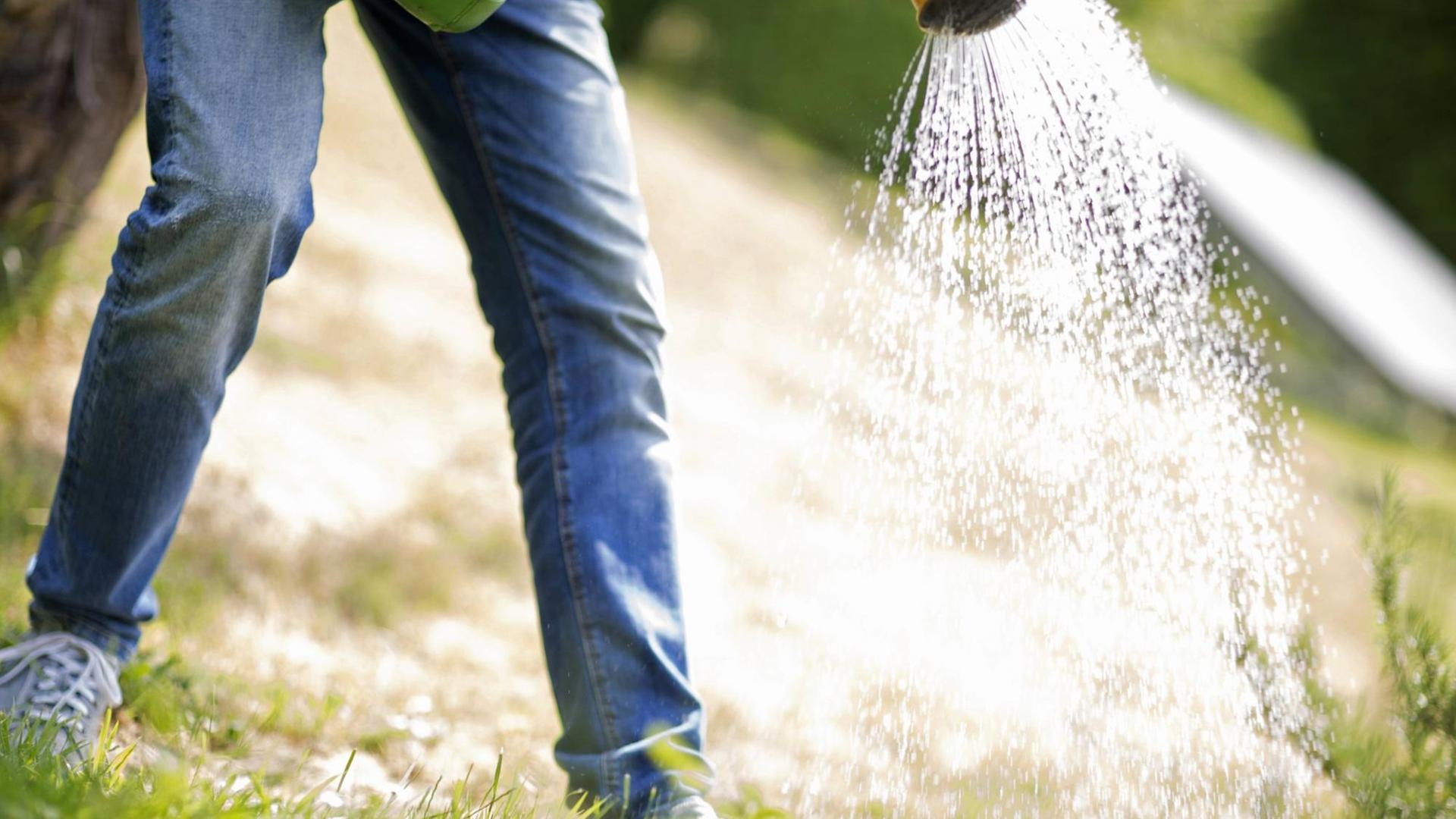 Man sieht zwei Beine, von oben wird ein Gartenschlauch gehalten, aus dem Wasser läuft.