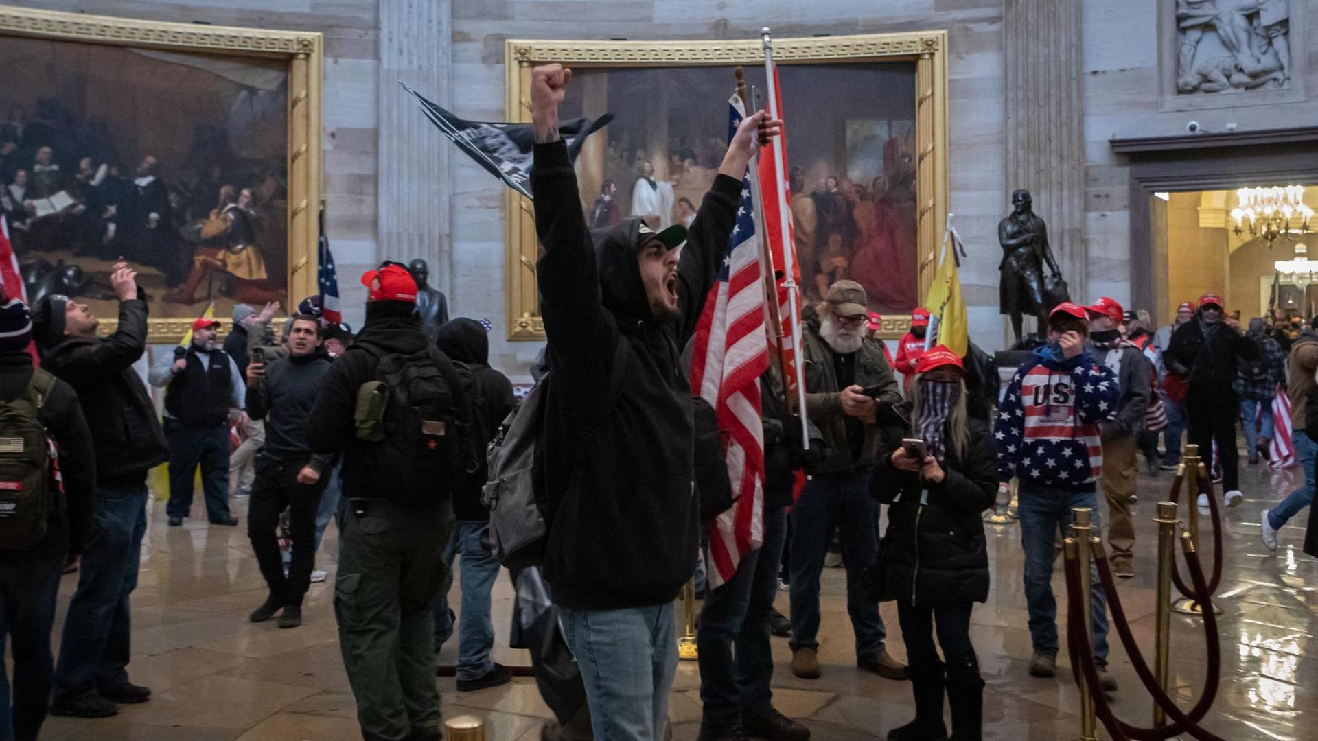 Ein Mob von Trump-Anhängern läuft durch eine Halle im Kapitol. Ein Mann in der Mitte hebt triumphierend die Arme.